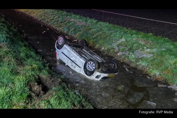 Auto ondersteboven in sloot op spiegelgladde weg, bestuurster met spoed naar ziekenhuis