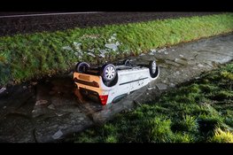 Auto ondersteboven in sloot op spiegelgladde weg, bestuurster met spoed naar ziekenhuis